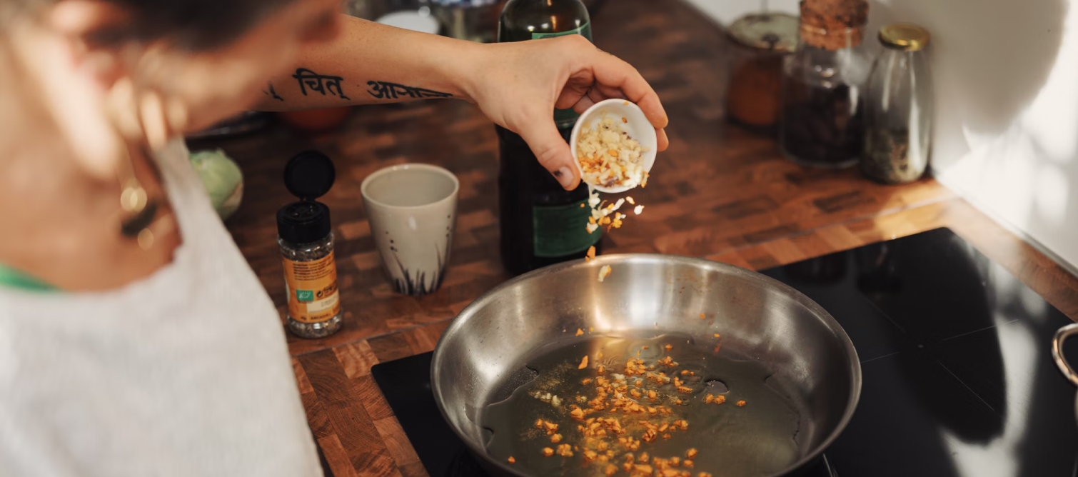 chef sprinkling chopped garlic into hot pan